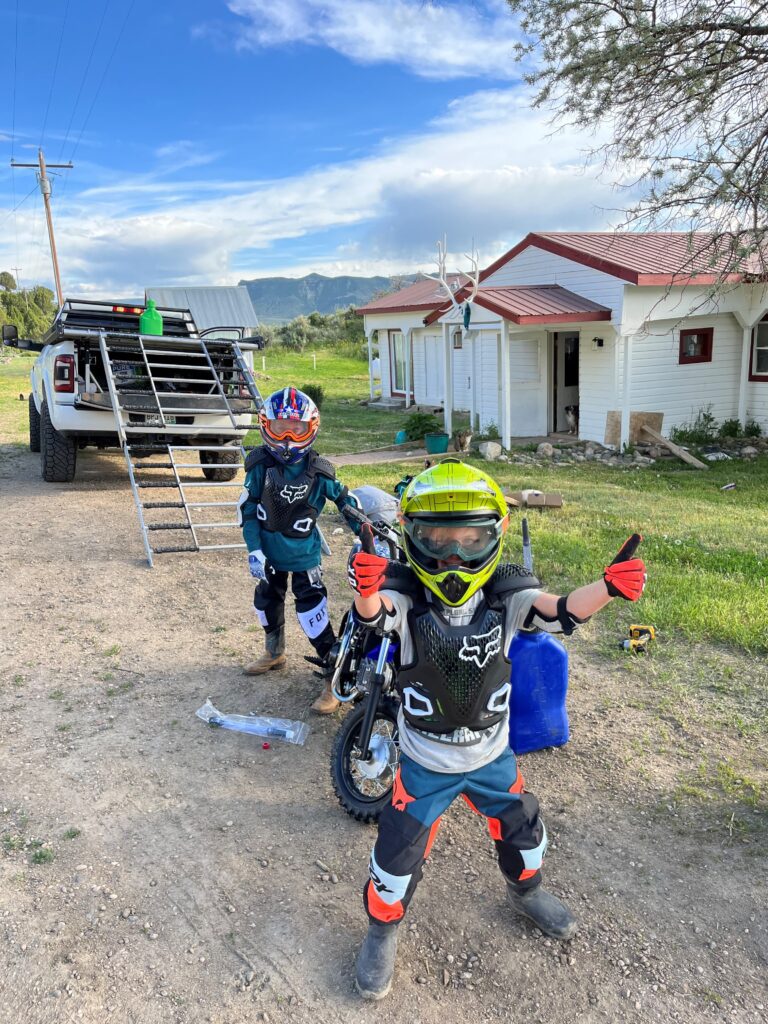 Two young boys are standing next to a dirt bike.